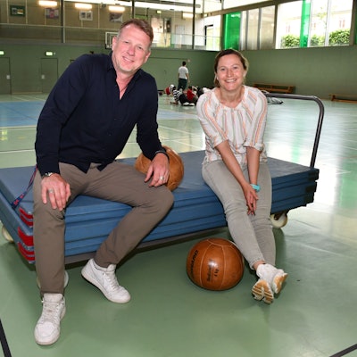 Sportlehrerin Diane Franzky und Schulleiter Carsten Balvin sitzen in der Sporthalle der Friedrich-Ebert-Realschule auf einem Mattenwagen.