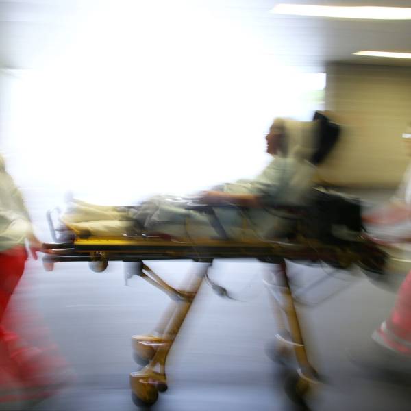 Rettungsassistenten liefern eine Notfallpatientin auf einer Trage in ein Krankenhaus ein.