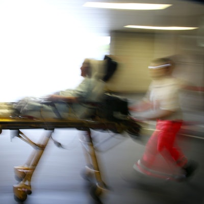 Rettungsassistenten liefern eine Notfallpatientin auf einer Trage in ein Krankenhaus ein.