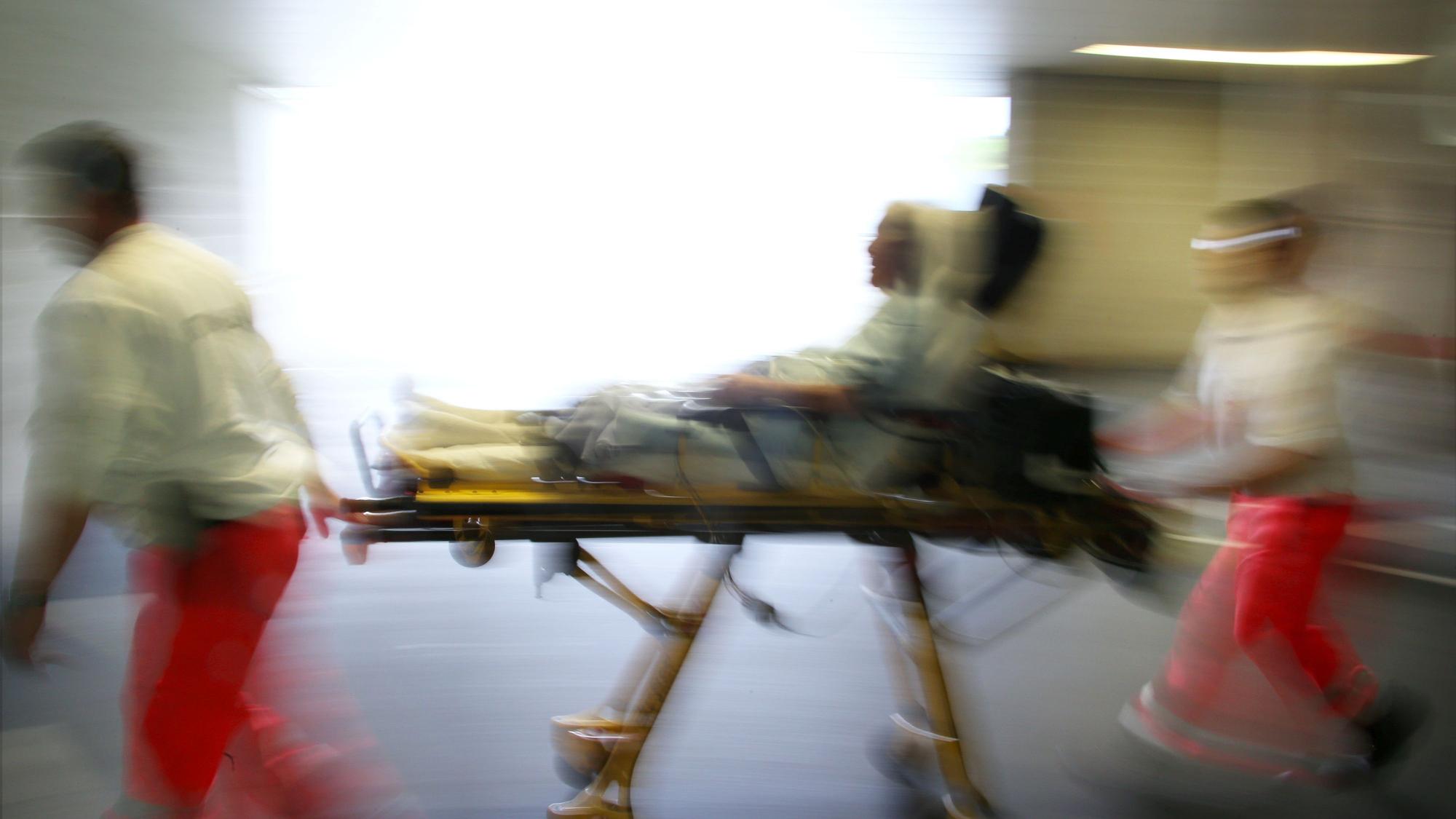 Rettungsassistenten liefern eine Notfallpatientin auf einer Trage in ein Krankenhaus ein.