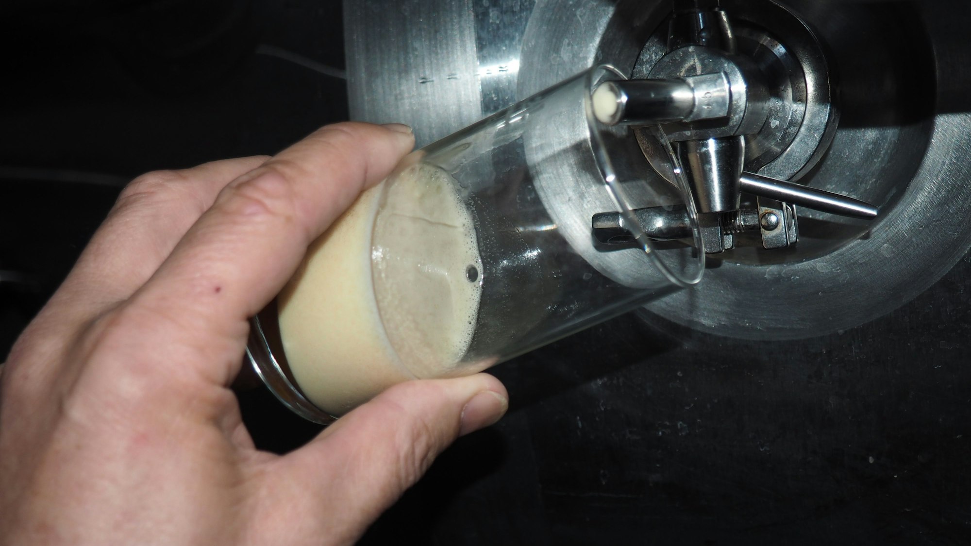 Eine Hand hält ein Glas unter ein Bierfass.