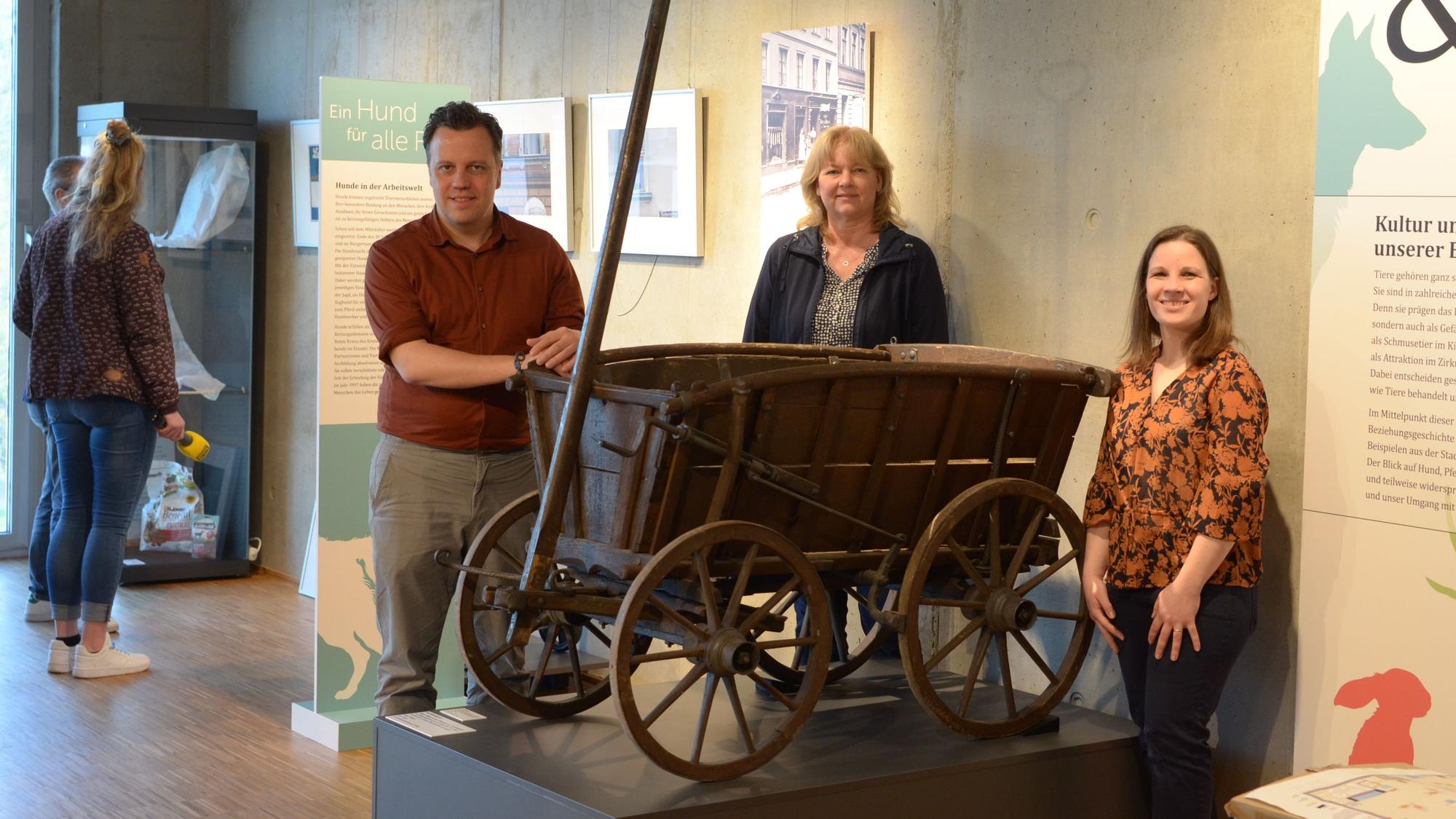 Euskirchens Bürgermeister Sacha Reichelt, Museumsleiterin Heike Lützenkirchen (M.) und ihre Mitarbeiterin Maja Kützemeier stehen im Stadtmuseum Euskirchen an einem Hundekarren.