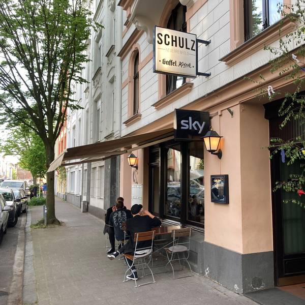 Außenansicht des Lokals Schulz in der Landmannstraße in Neuehrenfeld mit geschmücktem Maibaum und Gästen.