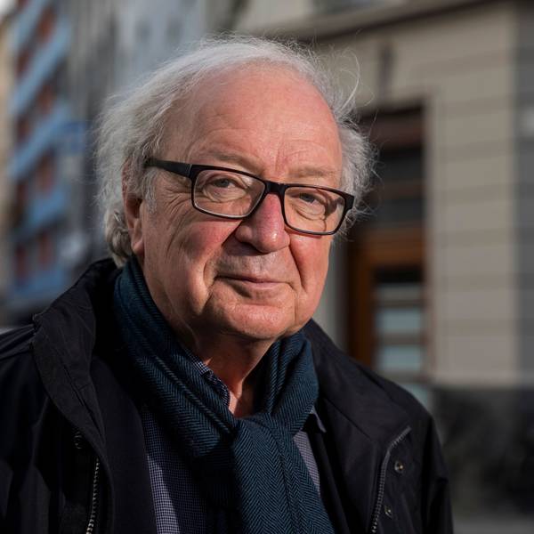 Der Journalist und Filmemacher Osman Okkan mit Brille, Hemd, Schal und Jacke und einer Kölner Straße im Hintergrund.
