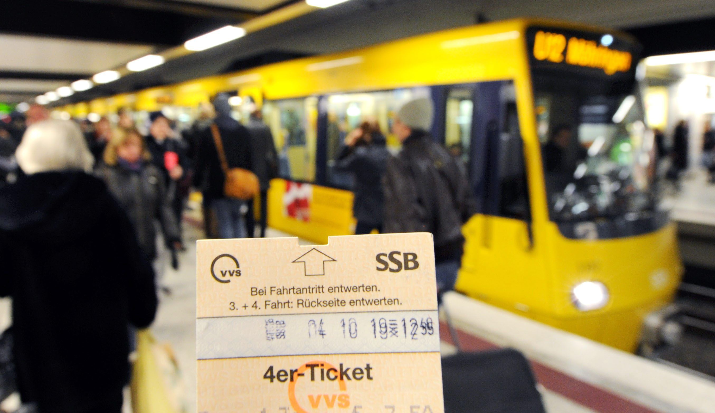 Eine Hand hält am am Hauptbahnhof ein Ticket vor einer Straßenbahn hoch.