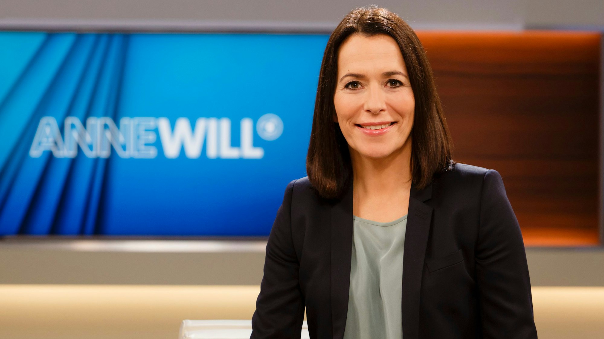 Anne Will sitzt im Studio auf dem Sofa