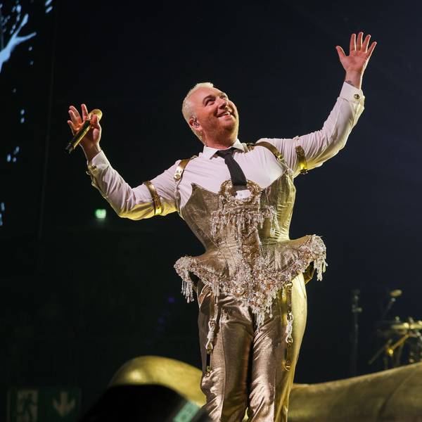 Sam Smith am 8. Mai 2023 in der Lanxess-Arena. Die nicht-binäre Person trägt ein goldenes Bustier über einem weißen Hemd und eine goldene Hose. Sie hält die Arme ausgestreckt und lächelt.