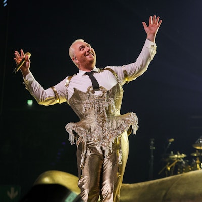 Sam Smith am 8. Mai 2023 in der Lanxess-Arena. Die nicht-binäre Person trägt ein goldenes Bustier über einem weißen Hemd und eine goldene Hose. Sie hält die Arme ausgestreckt und lächelt.