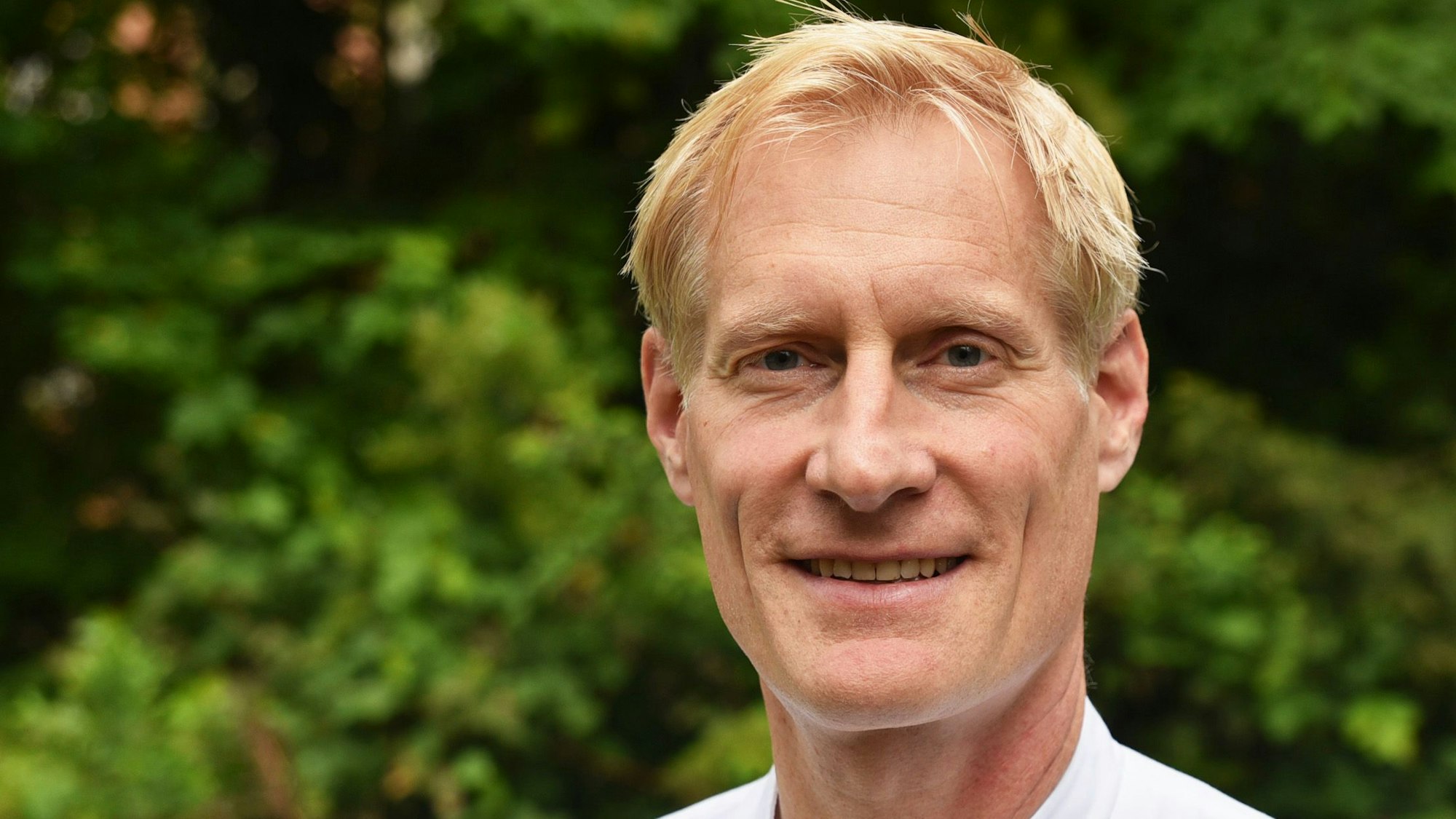 Christian Dohmen hat blondes Haar und lacht in die Kamera.
