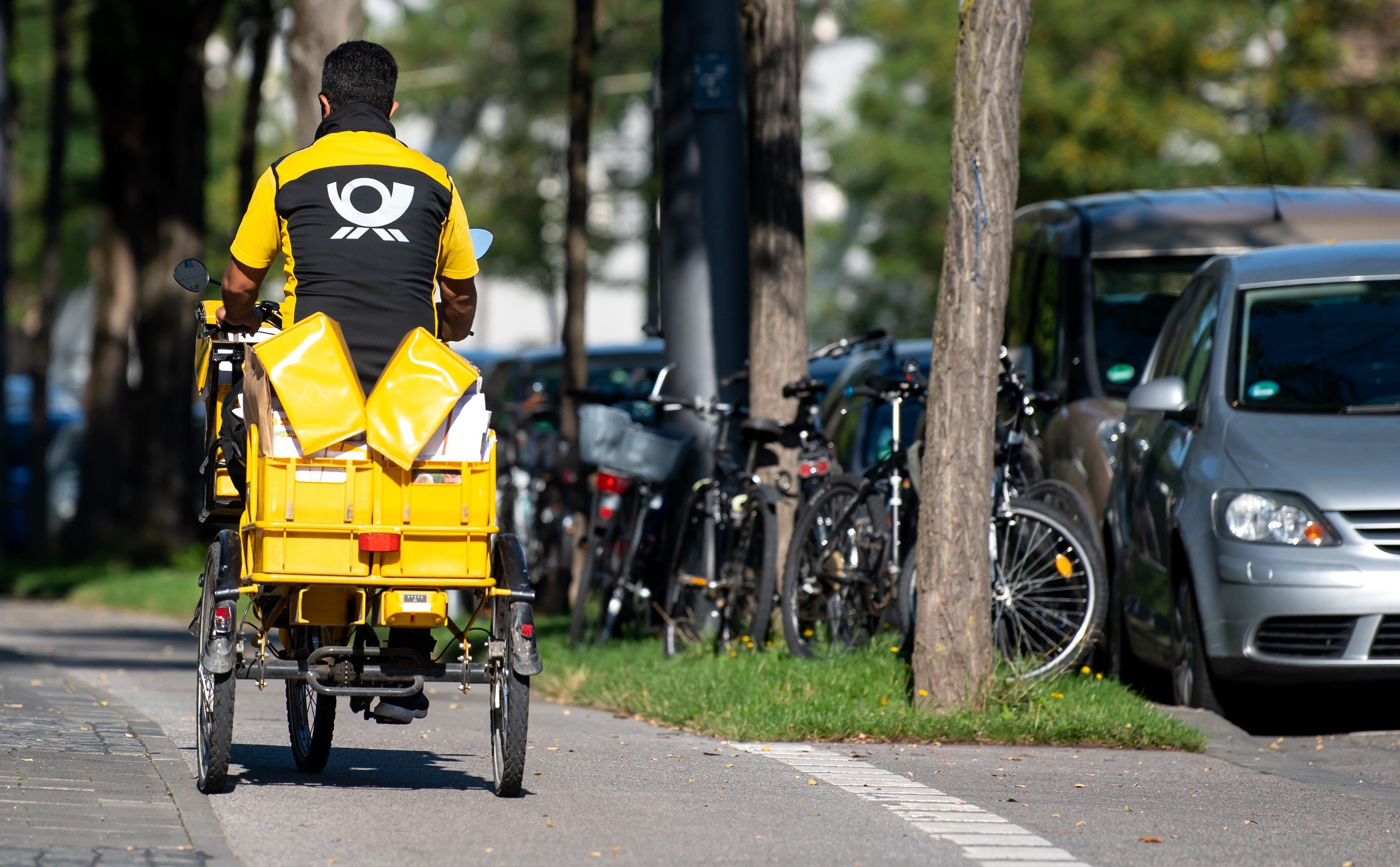 Ein Briefträger fährt mit seinem Fahrrad eine Straße entlang.