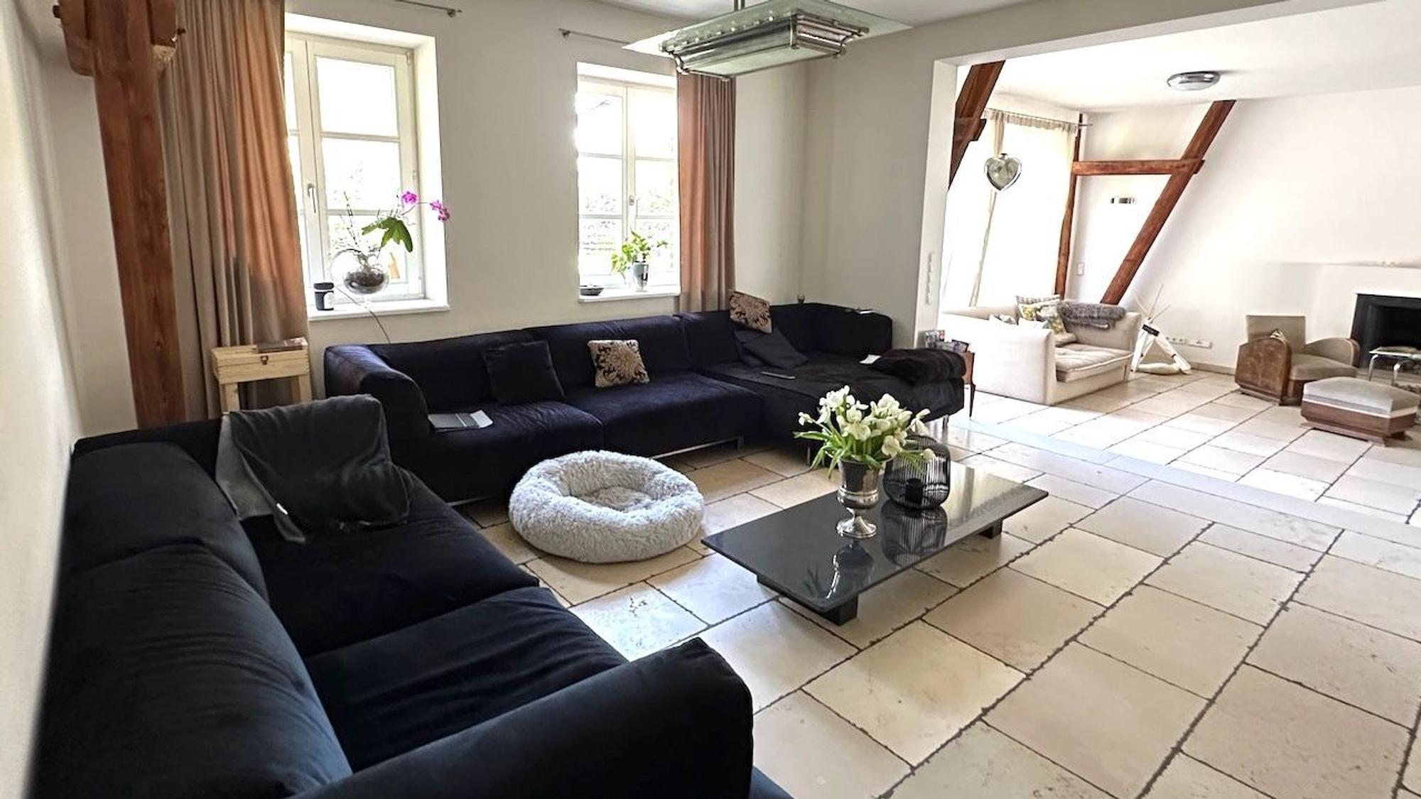 Zwei Sofas stehen in einem großzügigen Wohnraum mit hellem Natur-Steinboden.
