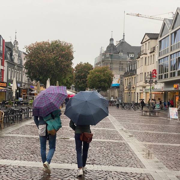 Das Foto zeigt die Fußgängerzone in Brüh. Zwei Personen gehen über die Uhlstraße, sie tragen Schirme, weil es regnet.