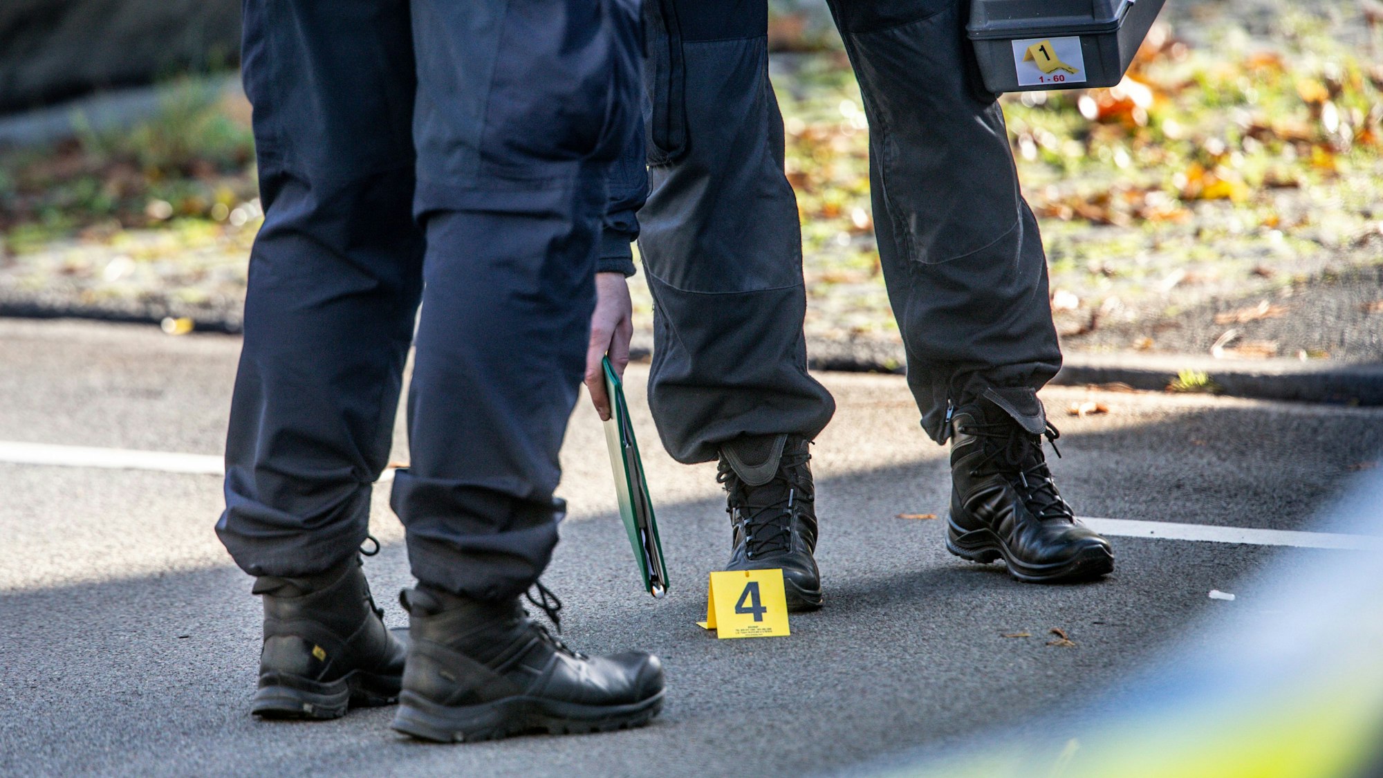 Polizisten sichern einen Einsatzort, nur die Beine der Polizeibeamten sind zu sehen, dazu eine gelbe Ortsmarkierung mit einer Vier darauf.