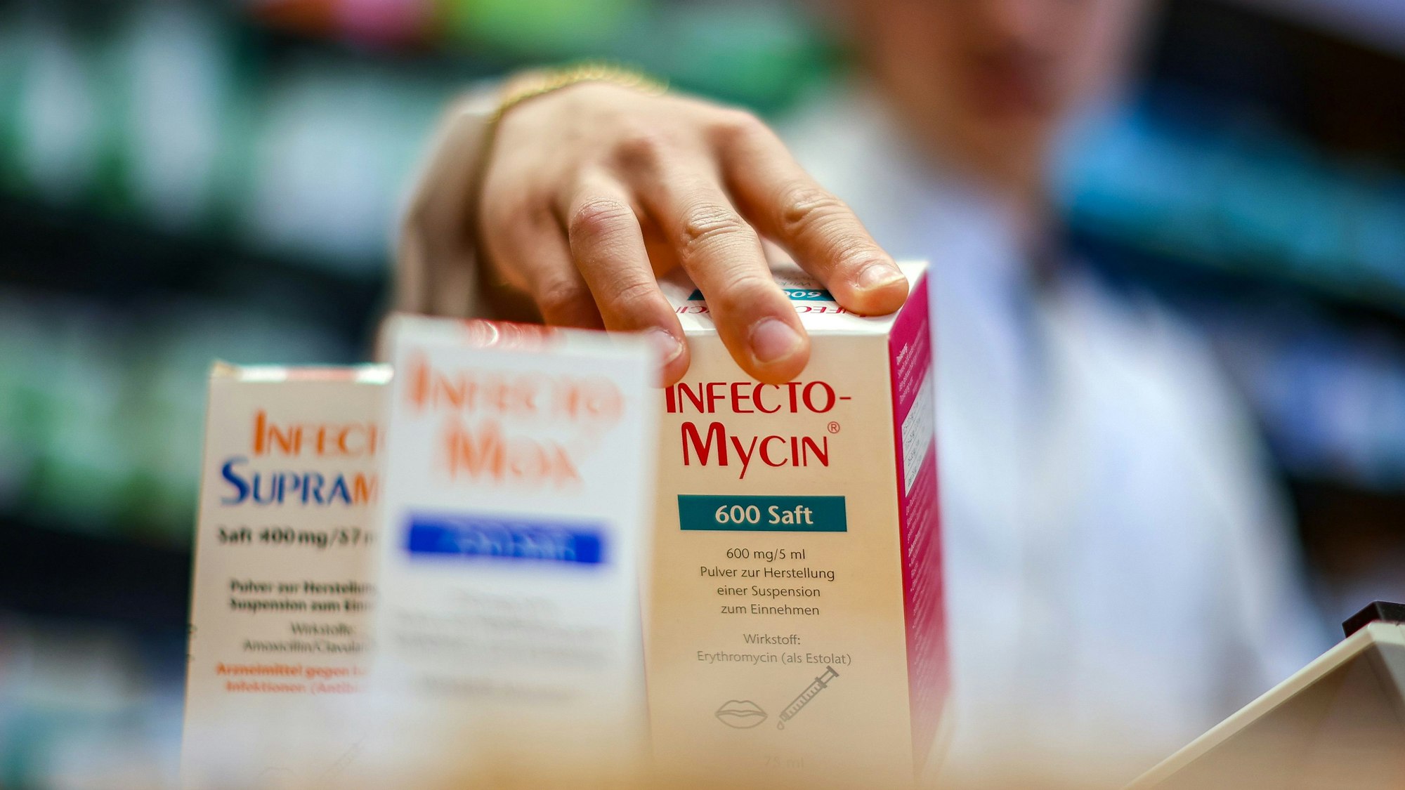 Eine menschliche Hand greift nach drei Medikamentenpackungen.