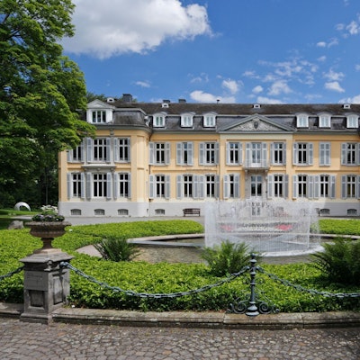 gelbes Schloss mit Park und Springbrunnen im Vordergrund