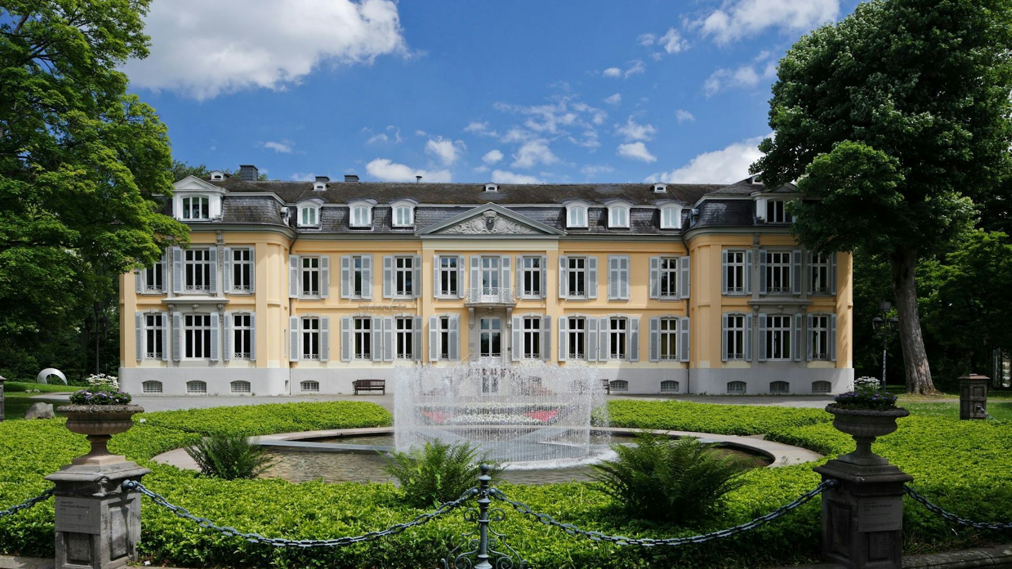 gelbes Schloss mit Park und Springbrunnen im Vordergrund