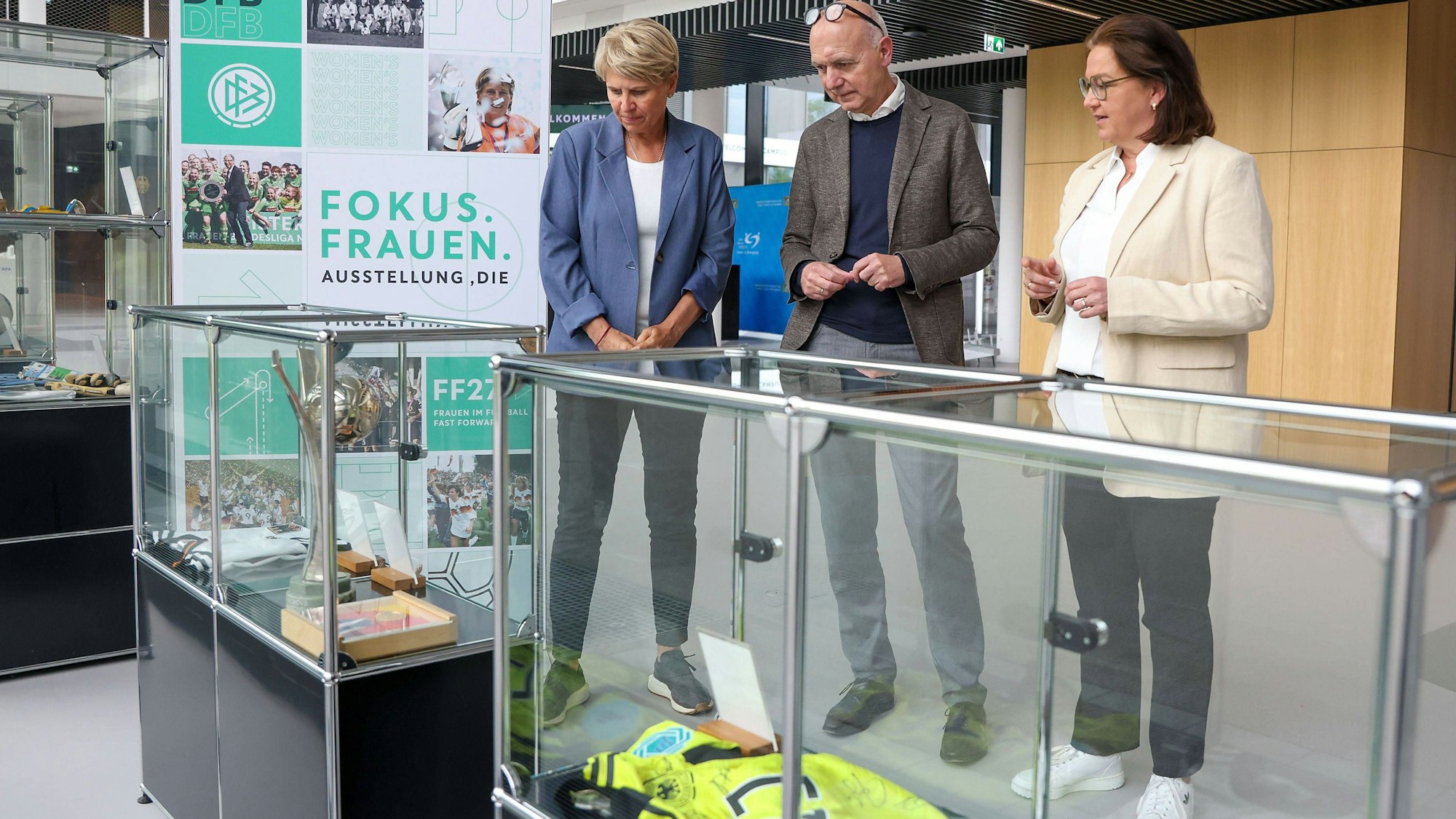 Doris Fitschen, Gesamtkoordinatorin Strategie FIFA Frauen-WM 2027, DFB-Präsident Bernd Neuendorf und DFB-Generalsekretärin Heike Ullrich schauen sich die Ausstellung zur Geschichte des Frauenfußballs an.
