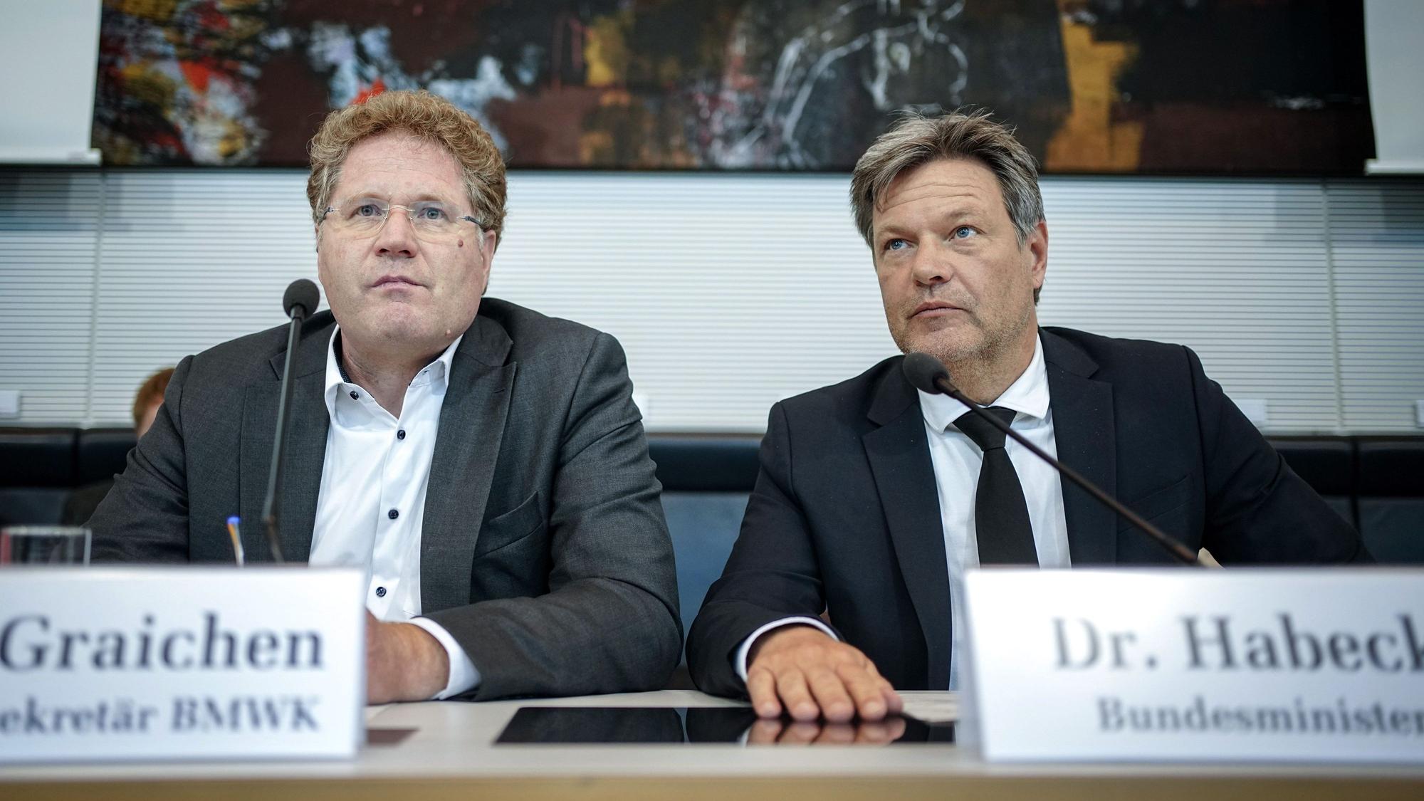 Bundeswirtschaftsminister Robert Habeck (r) und Staatssekretär Patrick Graichen sitzen nebeneinander an einem Tisch, vor Ihnen Schilder mit ihren Namen und ihrer Position. Beide schauen ernst, Graichen geradeaus, Habeck nach links. Hinter ihnen an der Wand hängt ein Gemälde mit vorwiegend dunklen Farben.