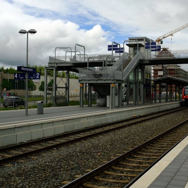 Der Blick auf die Fußgängerbrücke im Mechernicher Bahnhof, in dem ein Regionalzug hält.