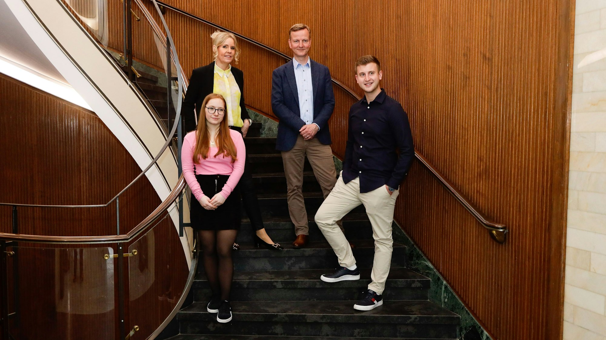 Zwei Männer und zwei Frauen, die auf einer Wendeltreppe stehen und die Kamera lächeln