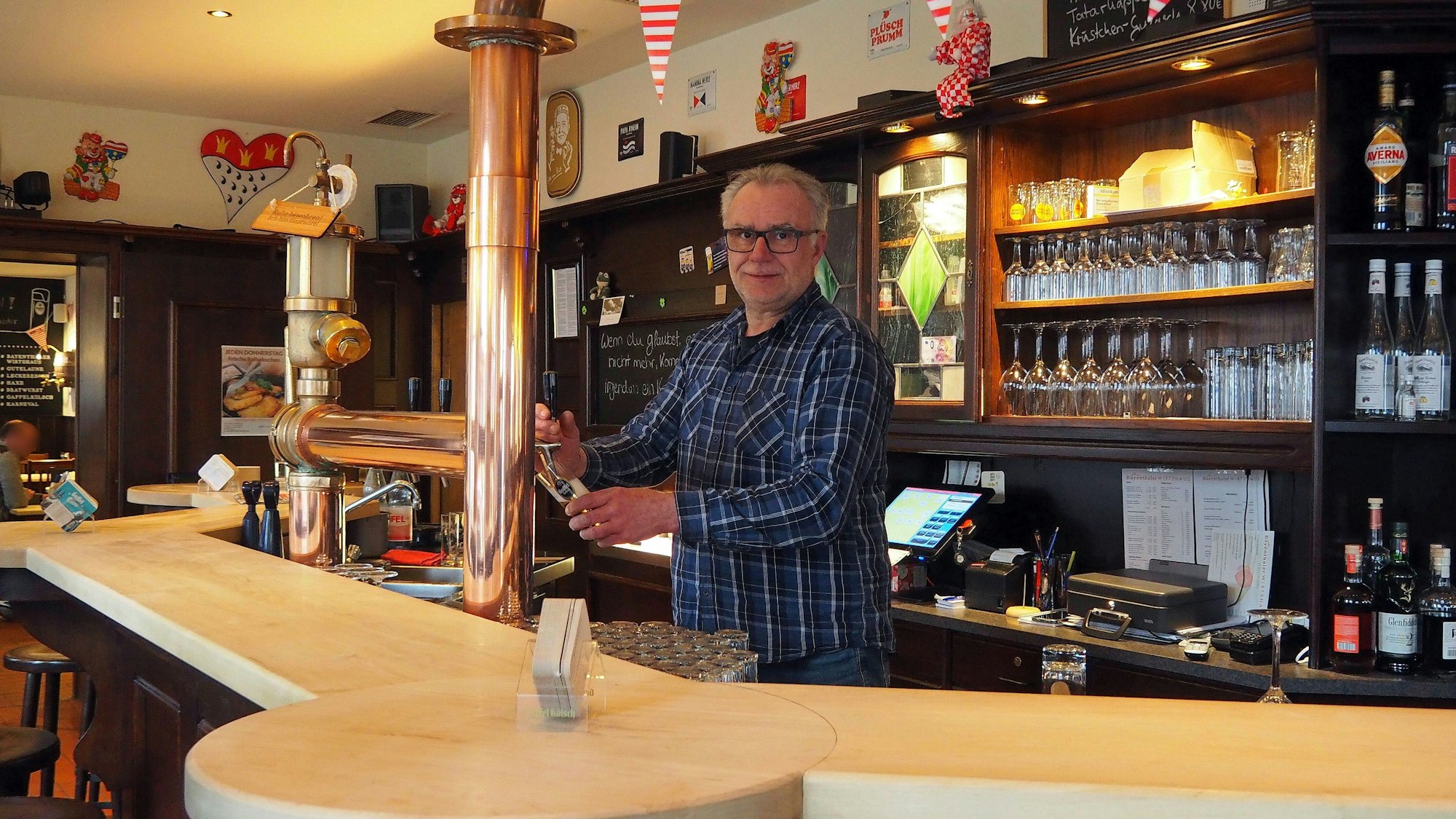Der Wirt steht hinter der Theke und zapft ein Kölsch.