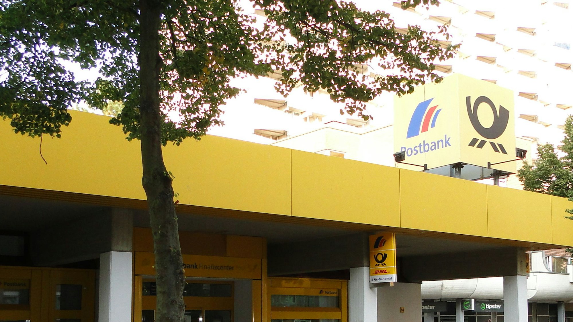 Die Filiale von Außen, ein Baum steht vor dem Eingang.