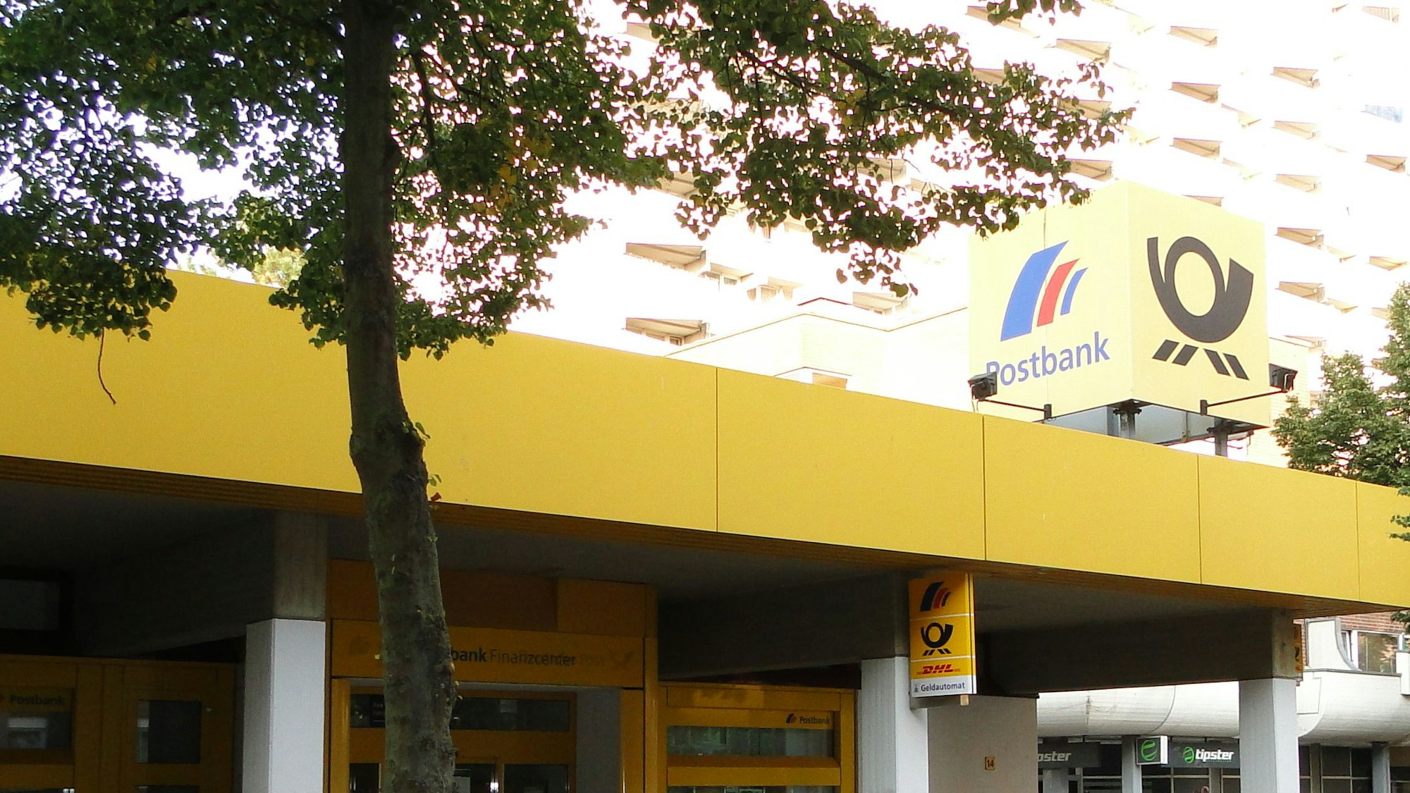 Die Filiale von Außen, ein Baum steht vor dem Eingang.