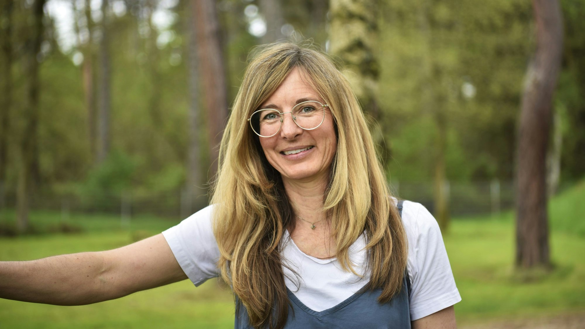 Corinne Rasky steht auf einer wiese mit Bäumen im Hintergrund.