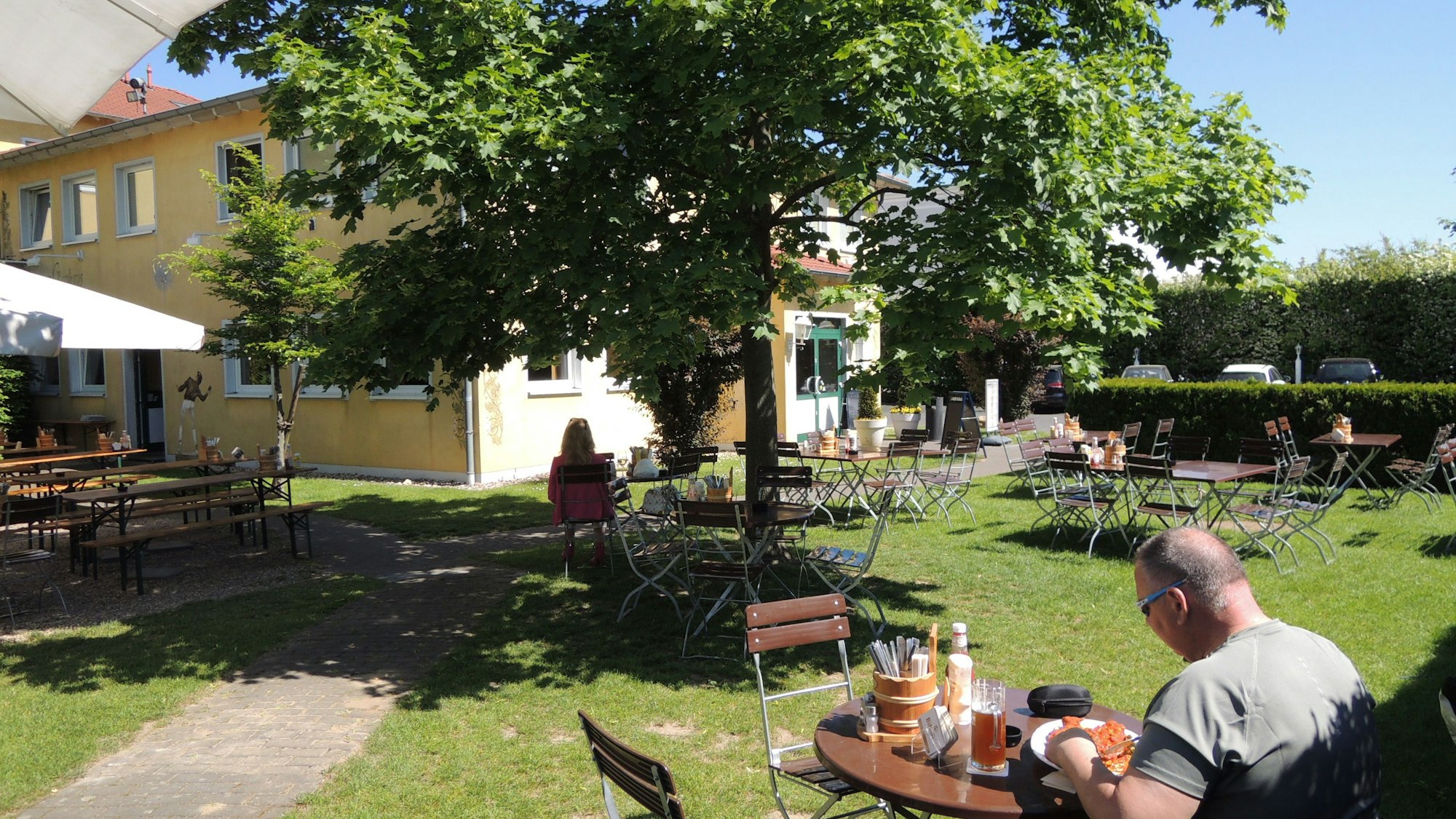 Ein Mann sitzt an einem Tisch und verzehrt ein Gericht. Im Garten stehen weitere Tische.
