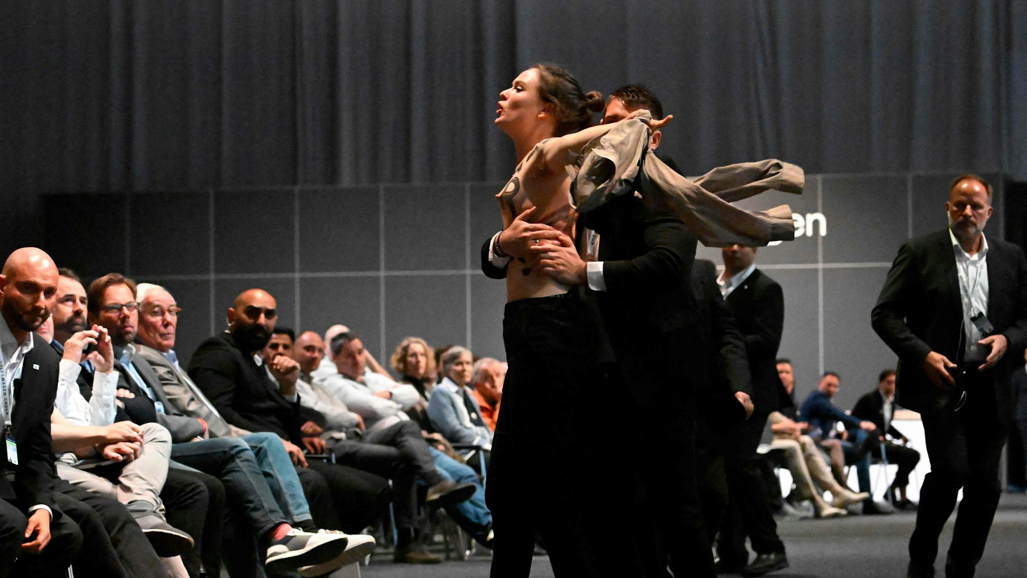 Eine halbnackte Aktivistin wird bei der VW-Hauptversammlung in Berlin von Sicherheitskräften aus dem Saal gebracht.