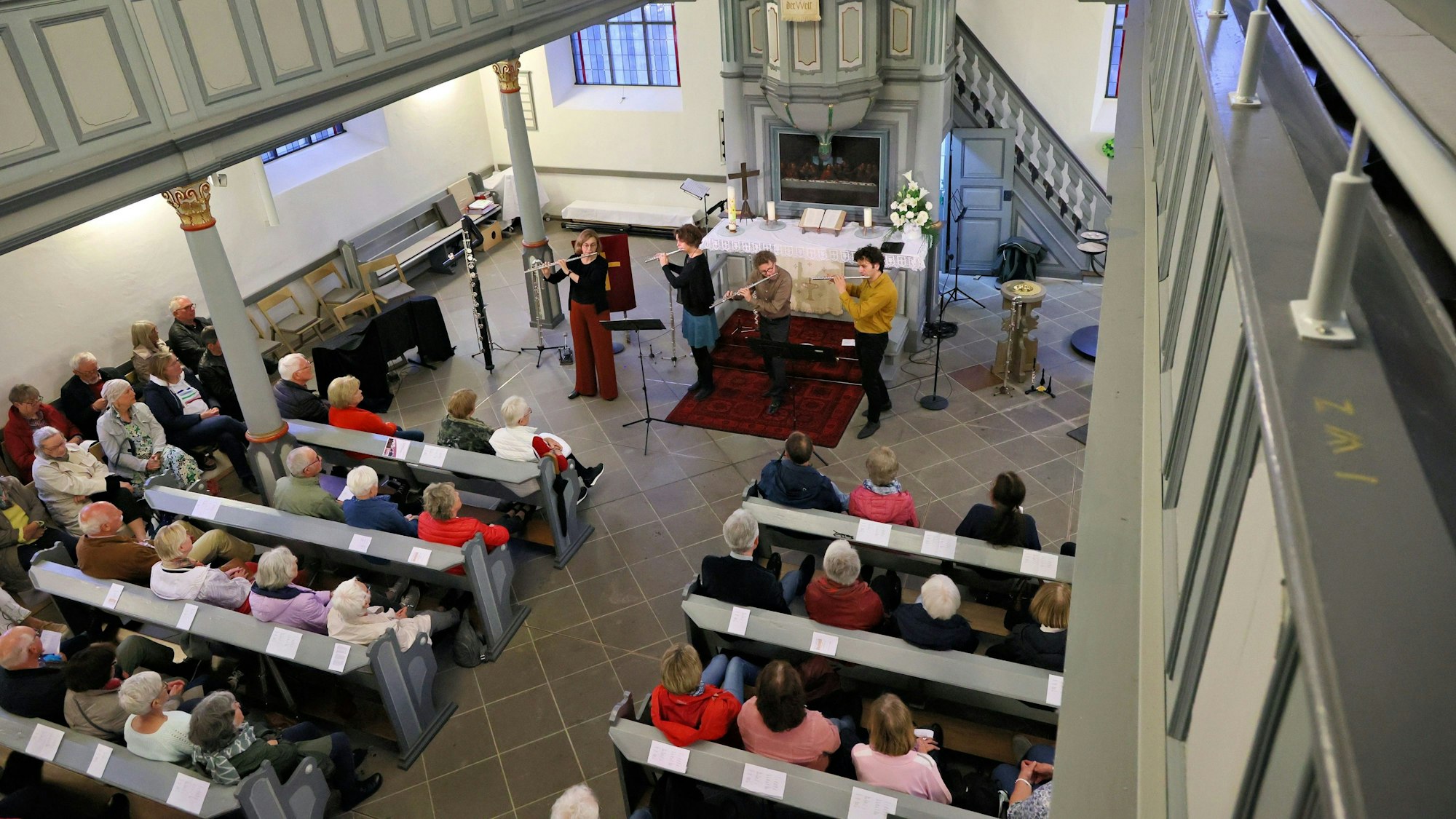 Das vierköpfige Flötenensemble spielt in der Kirche, Menschen sitzen in den Bänken und hören zu.