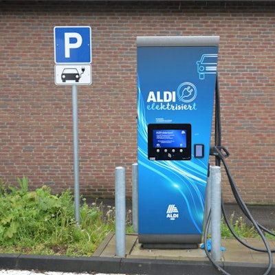 Eine E-Ladesäule mit der Aufschrift „Aldi“ steht vor einer Mauer.