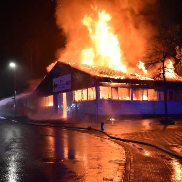 Eine Markthalle steht in Flammen. Ein Feuerwehrmann löscht.