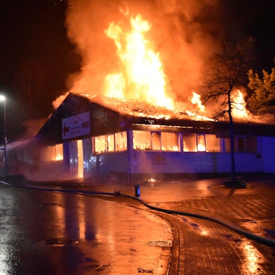 Eine Markthalle steht in Flammen. Ein Feuerwehrmann löscht.