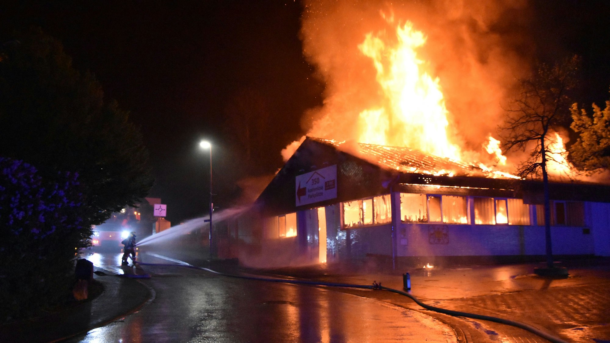 Eine Markthalle steht in Flammen. Ein Feuerwehrmann löscht.