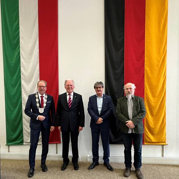 Das Foto zeigt Bürgermeister Volker Mießeler und die neuen Bergheimer Ehrenbürger Johannes Hübner, Helmut Paul und Peter Hirseler. Sie stehen vor den Flaggen von NRW und Deutschland.