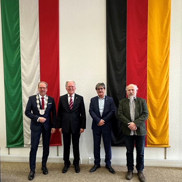 Das Foto zeigt Bürgermeister Volker Mießeler und die neuen Bergheimer Ehrenbürger Johannes Hübner, Helmut Paul und Peter Hirseler. Sie stehen vor den Flaggen von NRW und Deutschland.
