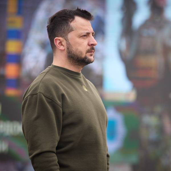 Der ukrainische Präsident Wolodymyr Selenskyj im Seitenprofil, er steht vor einem Plakat auf dem ein ukrainischer Soldat zu sehen ist.