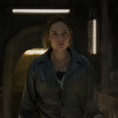 Eine Frau steht in Arbeitskleidung auf einer Stahlbrücke.