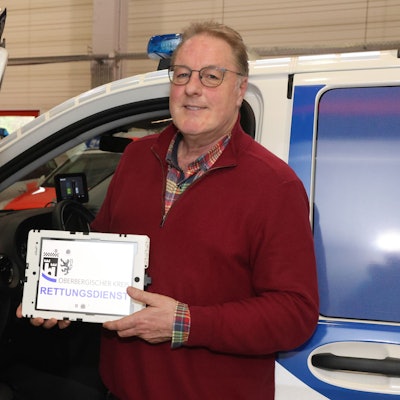 Zu sehen ist ein Mann mit einem Tablet vor einem Notarzteinsatzfahrzeug.