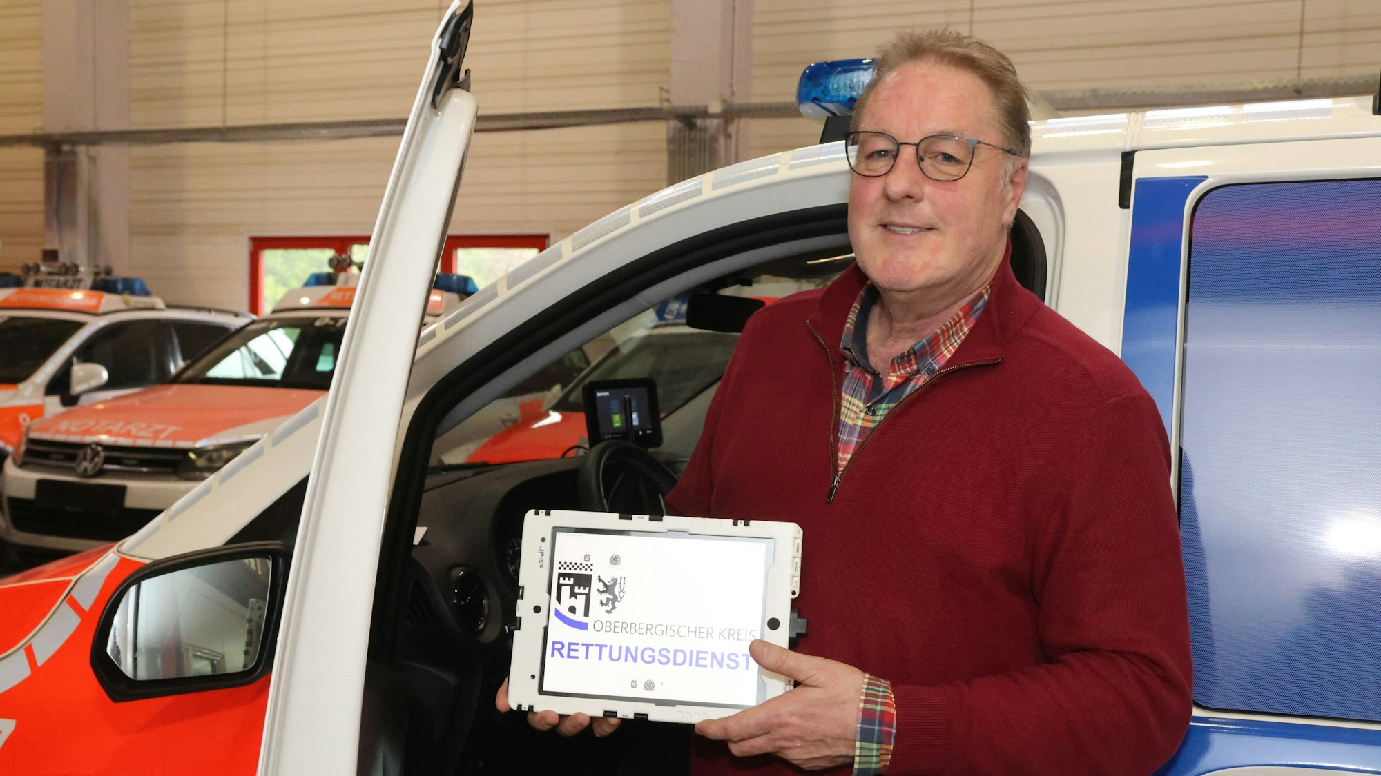 Zu sehen ist ein Mann mit einem Tablet vor einem Notarzteinsatzfahrzeug.