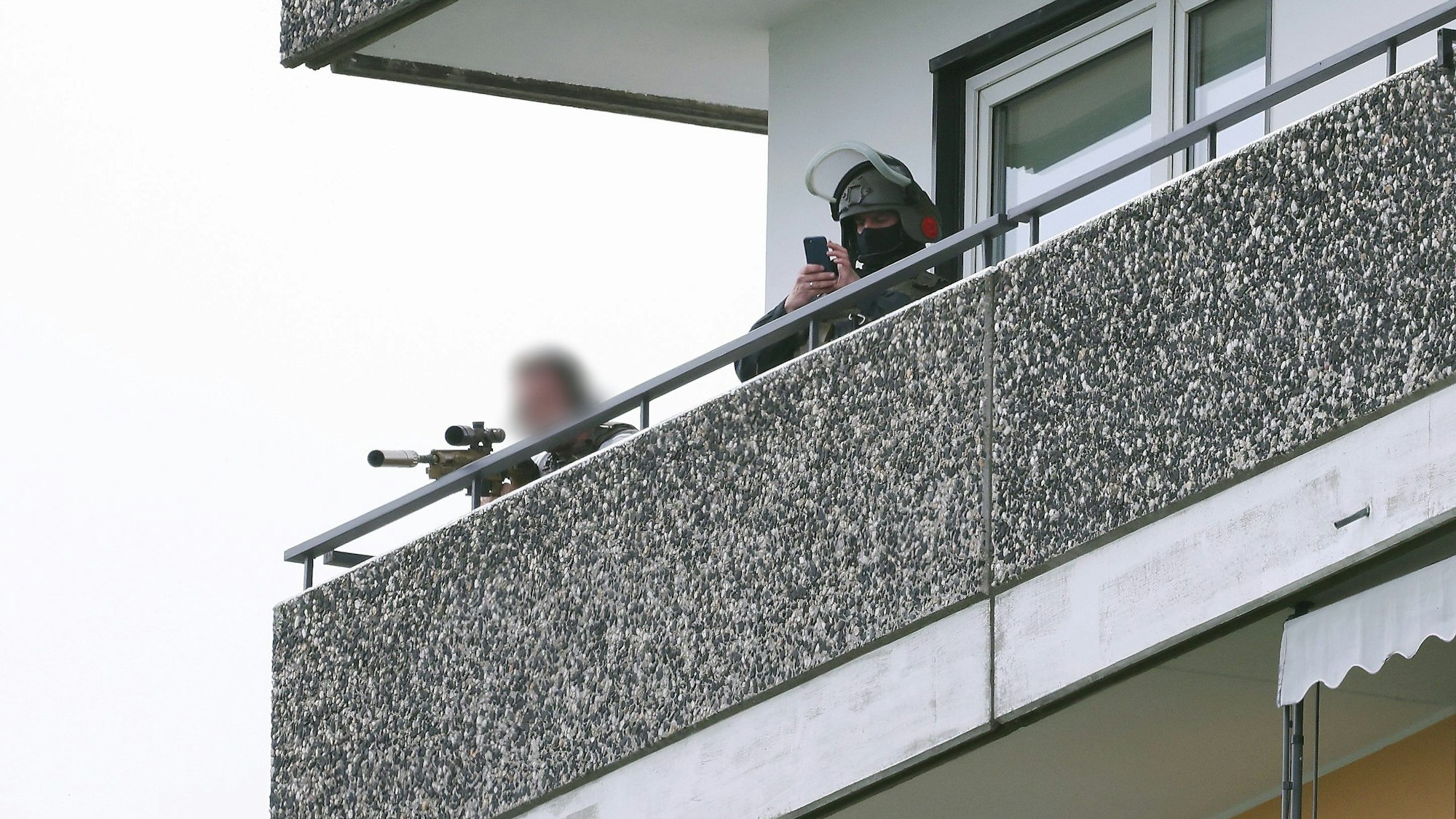 11.05.2023, Ratingen: Ein Polizeibeamter in Spezialausrüstung steht auf einem Balkon neben einem Kollegen und zielt mit einer Waffe. Bei einer Explosion in einem Hochhaus in Ratingen am Donnerstagvormittag wurden mehrere Menschen verletzt - darunter auch Polizisten und Einsatzkräfte der Feuerwehr. Das erfuhr die Deutsche Presse-Agentur aus Polizeikreisen. Foto: David Young/dpa - ACHTUNG: Die Person links im Bild wurde aus rechtlichen Gründen gepixelt +++ dpa-Bildfunk +++
