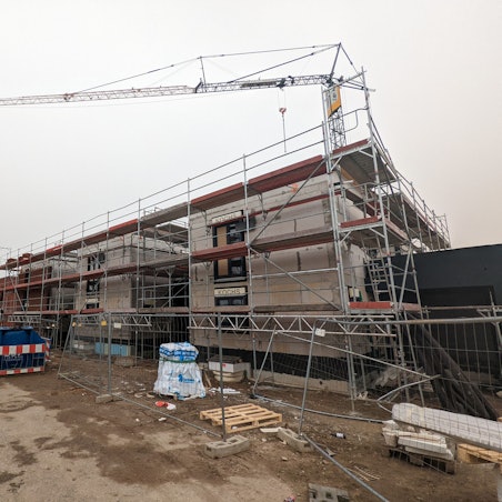 Ein Rohbau ist von Gerüst umrandet, dahinter steht ein Kran.