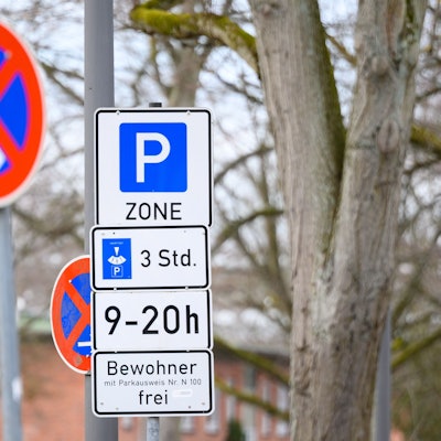 Schilder mit Hinweisen zu einer Bewohnerparkzone und eingeschränktem Halteverbot stehen an einer Straße.