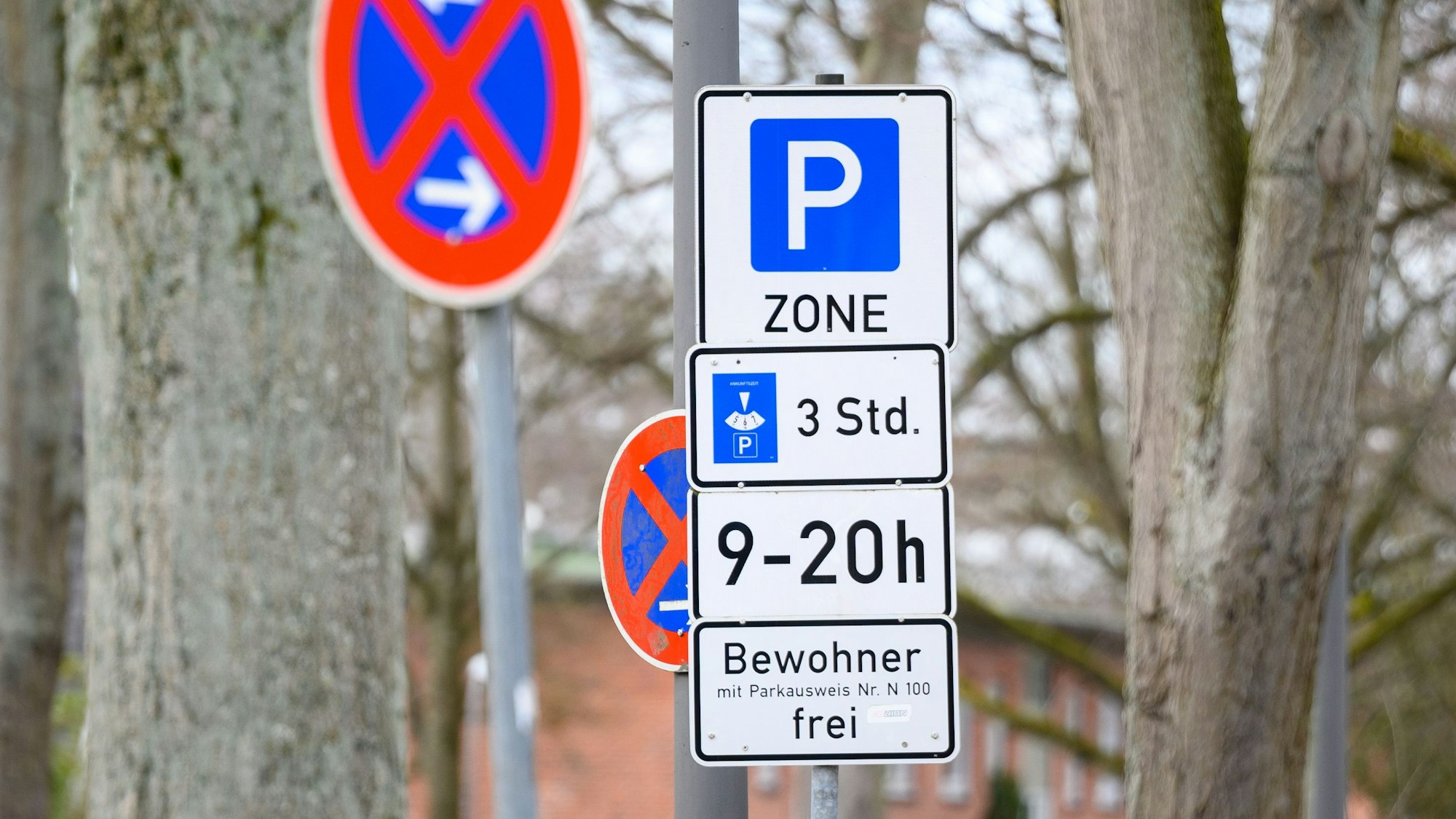 Schilder mit Hinweisen zu einer Bewohnerparkzone und eingeschränktem Halteverbot stehen an einer Straße.