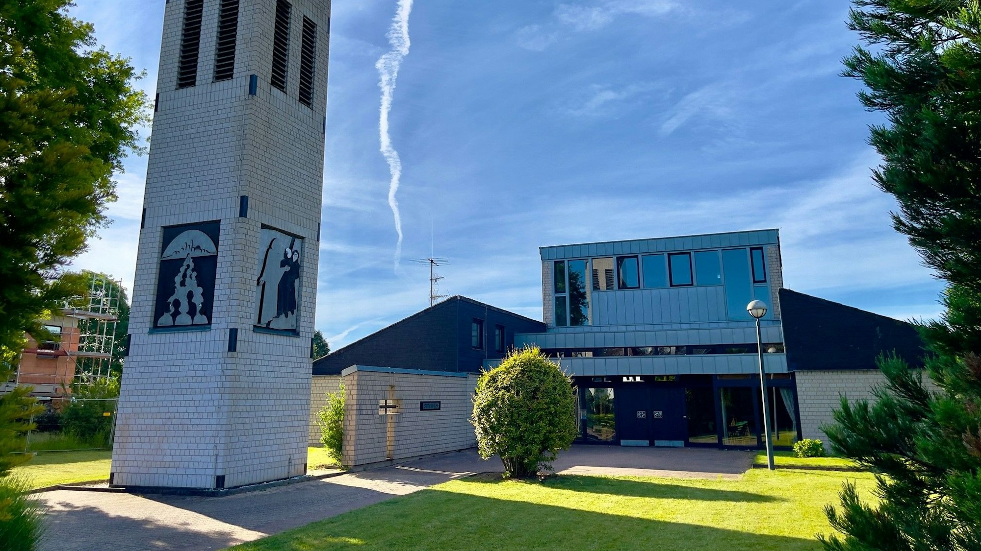 Blick auf die Kirche. Der Himmel ist blau und die Sonne scheint auf die grüne Wiese vor dem Eingang der Kirche.