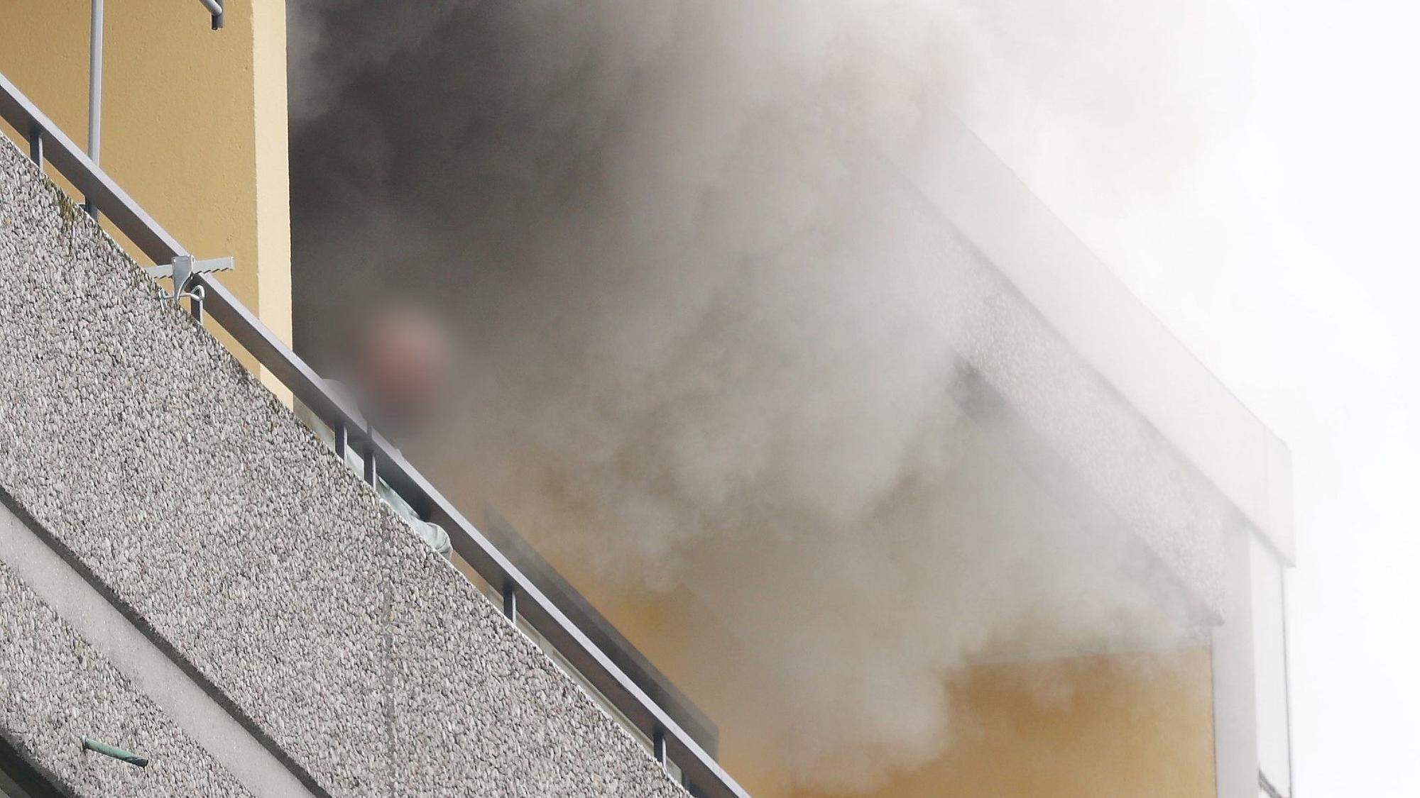 11.05.2023, Ratingen: Eine Person steht auf dem Balkon von einem Hochhaus, aus dem Rauch quillt. Bei einer Explosion in einem Hochhaus in Ratingen am Donnerstagvormittag wurden mehrere Menschen verletzt - darunter auch Polizisten und Einsatzkräfte der Feuerwehr. Das erfuhr die Deutsche Presse-Agentur aus Polizeikreisen. Foto: David Young/dpa - ACHTUNG: Die Perso wurde aus rechtlichen Gründen gepixelt +++ dpa-Bildfunk +++