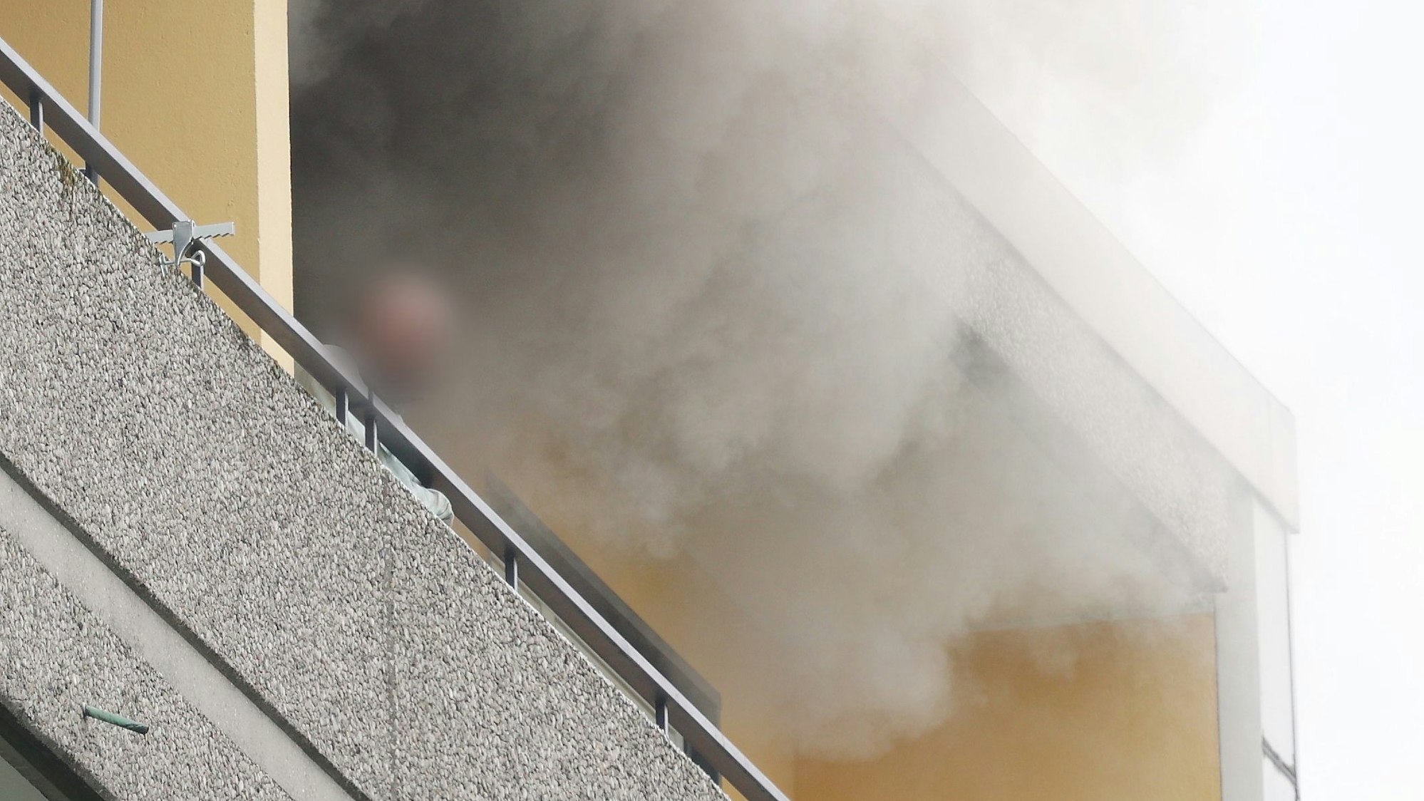 11.05.2023, Ratingen: Eine Person steht auf dem Balkon von einem Hochhaus, aus dem Rauch quillt. Bei einer Explosion in einem Hochhaus in Ratingen am Donnerstagvormittag wurden mehrere Menschen verletzt - darunter auch Polizisten und Einsatzkräfte der Feuerwehr. Das erfuhr die Deutsche Presse-Agentur aus Polizeikreisen. Foto: David Young/dpa - ACHTUNG: Die Perso wurde aus rechtlichen Gründen gepixelt +++ dpa-Bildfunk +++