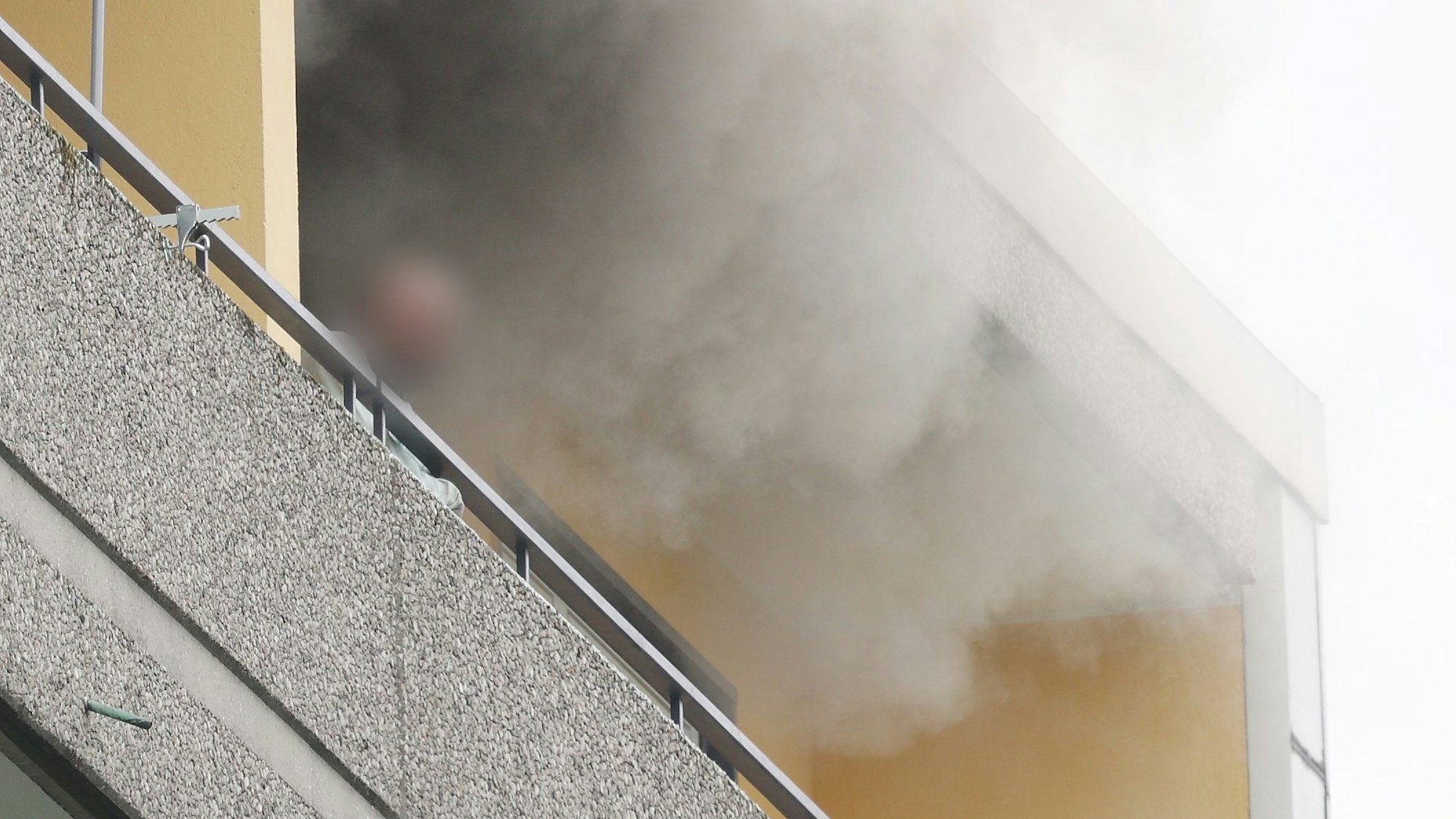 11.05.2023, Ratingen: Eine Person steht auf dem Balkon von einem Hochhaus, aus dem Rauch quillt. Bei einer Explosion in einem Hochhaus in Ratingen am Donnerstagvormittag wurden mehrere Menschen verletzt - darunter auch Polizisten und Einsatzkräfte der Feuerwehr. Das erfuhr die Deutsche Presse-Agentur aus Polizeikreisen. Foto: David Young/dpa - ACHTUNG: Die Perso wurde aus rechtlichen Gründen gepixelt +++ dpa-Bildfunk +++