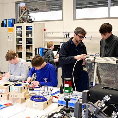 Auszubildende arbeiten in einer Werkstatt. Ein Ausbildungsleiter erklärt das Vorgehen.